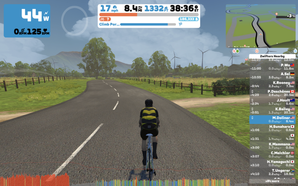 Screenshot of the Zwift Mac application, showing a rendered graphics of a cyclist riding on a road with power, heart rate, and time stats at the top.